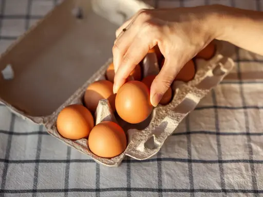 Dłoń wybiera jajko z wytłoczki. Zastanawiasz się, ile kcal ma jajko? To zdrowa przekąska!