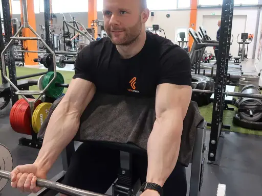 Mann trainiert Bizeps mit Langhantel im Fitnessstudio. Deutlich sichtbare Muskeln beim Bizeps dehnen.