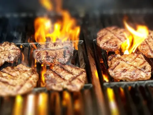 Flera saftiga hamburgare grillas över öppna lågor. Doften av sommar och grillning sprider sig.
