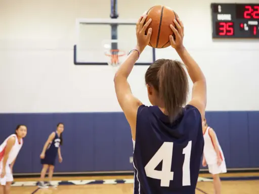 Ragazza con palla da basket, un ottimo sport per bambini iperattivi. In campo, altre giocatrici si preparano.
