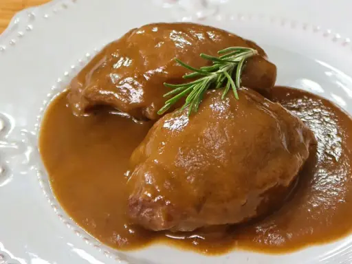 Deliciosas carrilleras de cerdo estofadas en salsa, coronadas con una ramita de romero fresco.