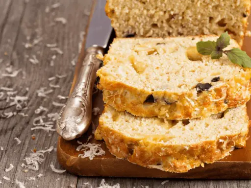 Pokrojona babka z cukinii z ziołami i serem, ułożona na desce, obok nóż.
