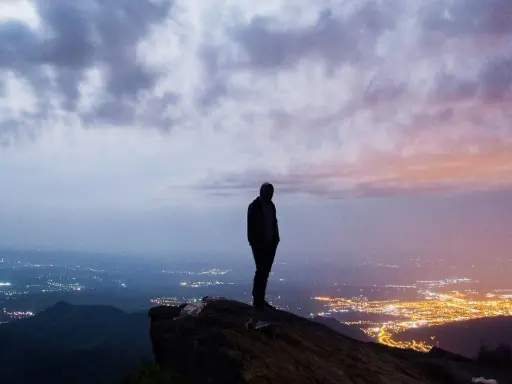 Silhouette di una persona su una rupe, con una città illuminata in lontananza. Un momento che fa amarcord, pensando a chi siamo e dove andiamo.