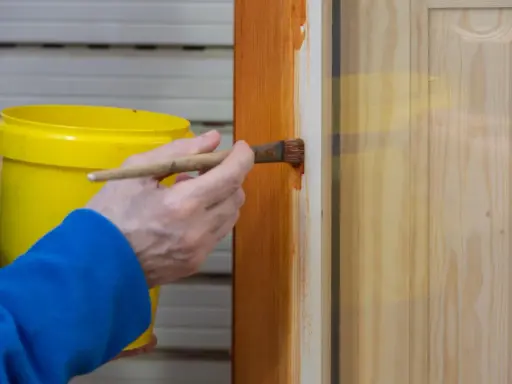 Persona aplica barniz a puerta de madera con brocha. Aprende como pintar puertas de madera para un acabado perfecto.