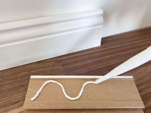 Kleber wird auf eine Sockelleiste aufgetragen, um sie an der Wand zu befestigen.