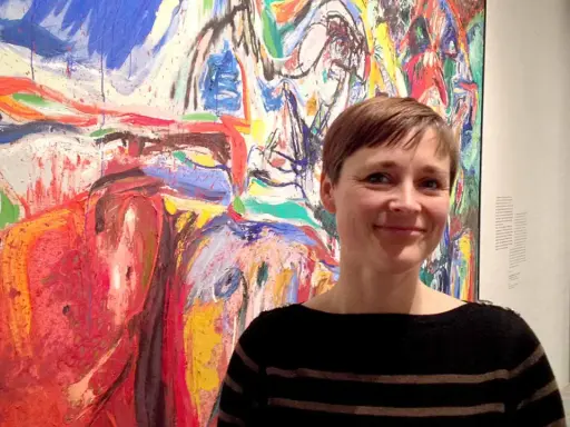 Kvinna ler framför en färgstark målning i Asger Jorns stil.