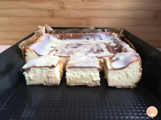 Pyszny sernik z mlekiem, pokrojony na kwadraty, polany białą polewą z czekoladowymi wzorami.