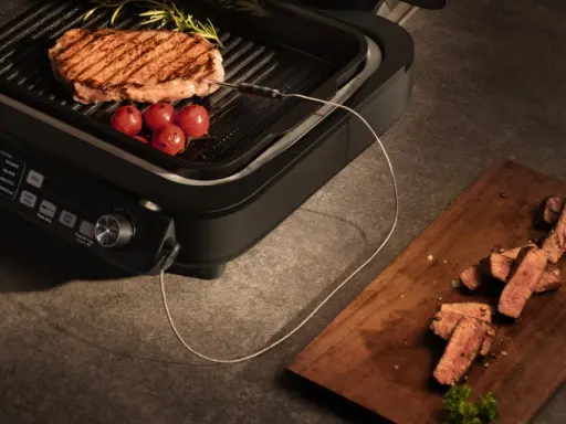 Idealne grillowanie na grillu elektrycznym. Soczysty stek z pomidorkami i rozmarynem, a obok pokrojone mięso na desce.