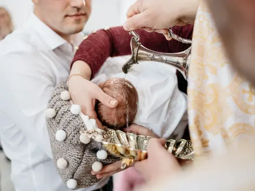 Woda święcona spływa na główkę dziecka podczas ceremonii na chrzcie.