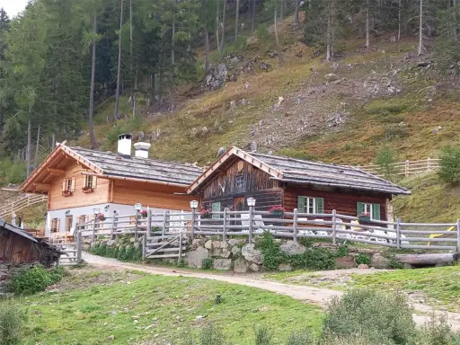 Tablander Alm a Parcines, con due baite in legno e recinzione, immerse nel verde di un pendio boscoso.