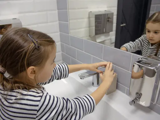 Niña se lava las manos en el baño, un gesto importante para la higiene y la prevención del toc en niños.