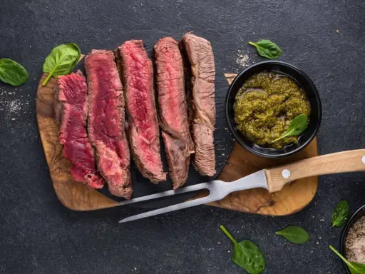 Saftiges, aufgeschnittenes Fleisch zum Grillen, serviert mit Kräutersauce und Gewürzen.