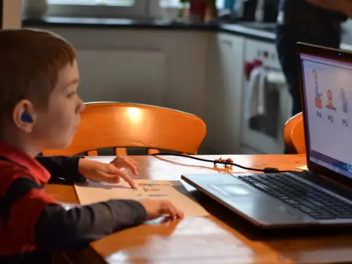 Chłopiec z niebieskim aparatem słuchowym ćwiczy wymowę sylab na lekcji logopeda online.