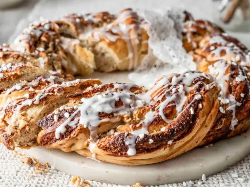 Ein goldbrauner nusskranz hefe, mit Zuckerguss und Perlen verziert, liegt auf einem Marmorsockel.