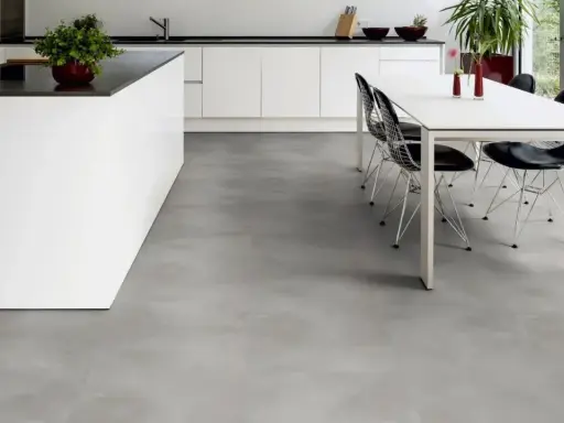 Cucina moderna con isola bianca e tavolo da pranzo. Il pavimento in LVT grigio effetto cemento completa l'ambiente minimalista.