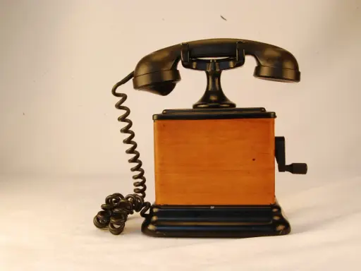 Stary telefon na korbkę z drewnianą obudową i czarną słuchawką.