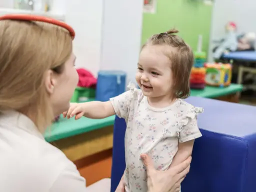 Uśmiechnięte dziecko wyciąga rączkę do terapeuty. To przykład, co to jest integracja sensoryczna – wspieranie rozwoju dziecka.