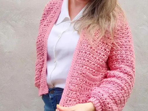 Mujer con un cardigan a crochet rosa, sobre una camisa blanca y jeans.