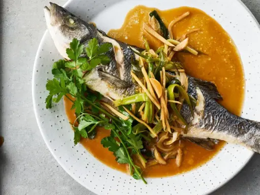 Ein ganzer Wolfsbarsch Fisch, gedünstet in einer würzigen Sauce mit Ingwer und Frühlingszwiebeln, garniert mit Koriander.