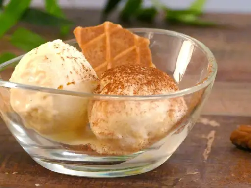 Dos bolas de helados caseros en un cuenco de cristal, espolvoreados con canela y acompañados de galletas.