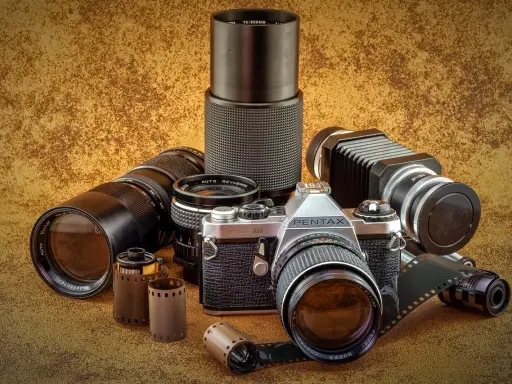 Kolekcja sprzętu fotograficznego: aparat Pentax JMC Super, obiektywy, mieszek i klisze.