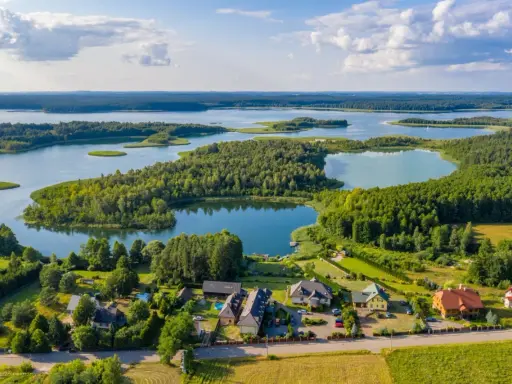 Malownicze góry i jezioro w jednym, otoczone zielenią. Domy z dachami w różnych kolorach, położone blisko wody.