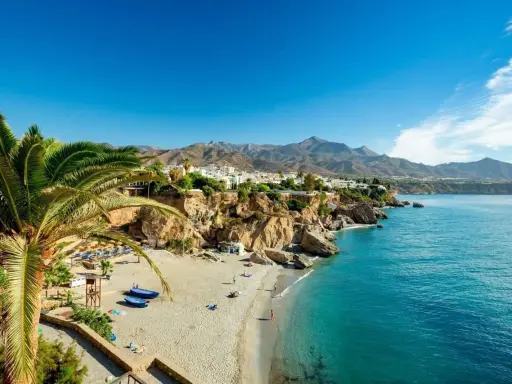 Sonnige playa de calahonda mit Palmen, weißem Sand, türkisfarbenem Meer und Bergen im Hintergrund.
