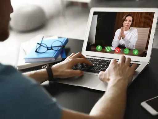 Mężczyzna prowadzi wirtualną superwizję przez laptopa. Na ekranie widać kobietę z dłońmi złożonymi w geście modlitwy.