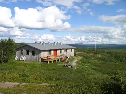 Kungsleden stugor i fjällandskap med molnig himmel. Enkel träbyggnad med veranda och flaggstång.