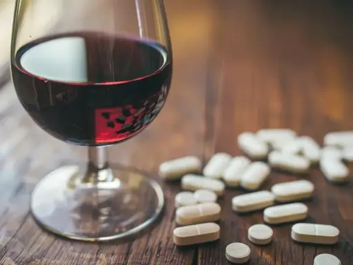 Kieliszek czerwonego wina obok garści tabletek. Leki przeciwzapalne a alkohol – potencjalne ryzyko interakcji.