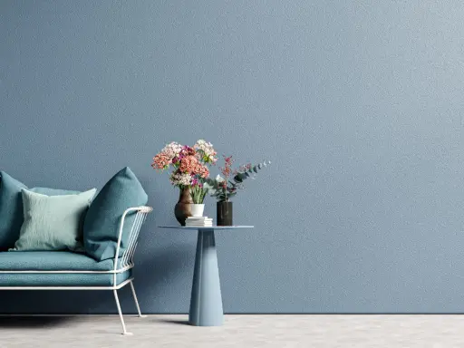 Divano blu petrolio e cuscini in tonalità pastello su sfondo azzurro polvere. Ottime idee colori pareti per un ambiente rilassante.
