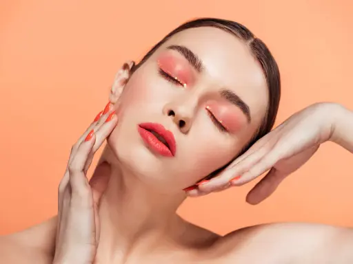 Maquillajes Euphoria: ojos con sombra coral brillante y labios rojos vibrantes, uñas a juego.