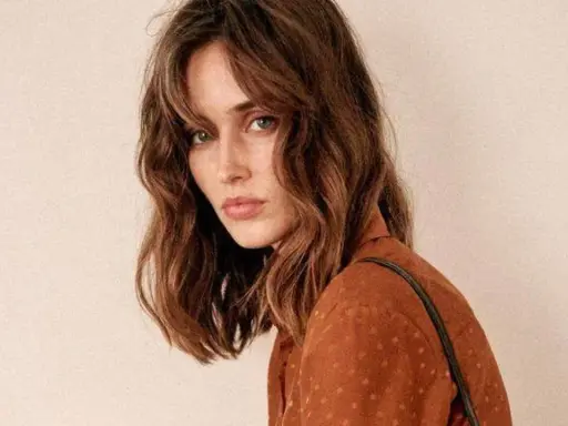 Mujer con un corte de pelo clavicut, ondas suaves y flequillo desfilado, luciendo un top marrón con lunares.