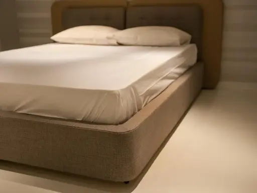 Un lit moderne avec un sommier tapissier, une base recouverte de tissu beige, prêt à accueillir un matelas blanc et des oreillers.