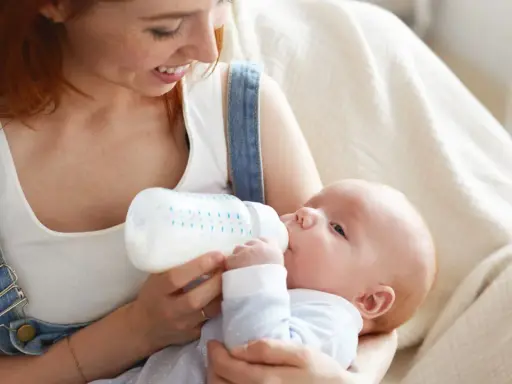 Mamma con capelli rossi nutre il suo neonato con latte artificiale ogni 2 ore. Il piccolo beve con gusto dalla bottiglia.