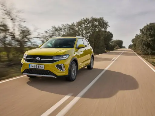 Un coche amarillo Volkswagen T-Cross circula por una carretera rural. ¿Cuánto se tarda en fabricar un coche? ¡Este parece listo para la carretera!