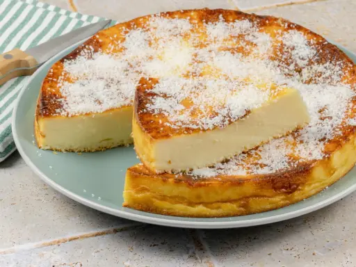 Un délicieux flan coco, saupoudré de noix de coco râpée, est servi sur une assiette. Une part est coupée et posée sur le dessus.