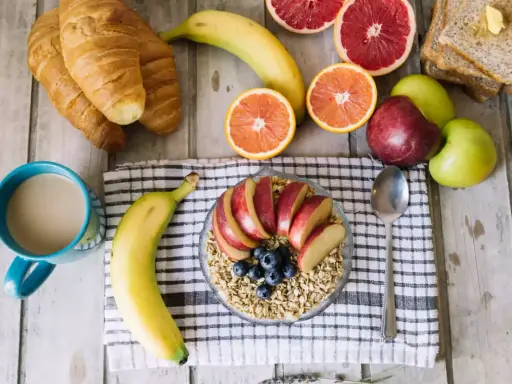 Pyszne i lekkostrawne śniadanie: owsianka z jabłkiem i jagodami, banan, croissanty, cytrusy i kawa.