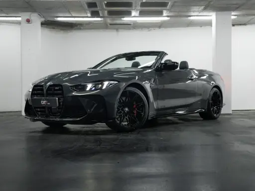 Un elegante BMW M4 negro descapotable, con sus luces LED encendidas, posa en un garaje.