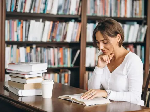 Donna legge in biblioteca, circondata da libri. La sua concentrazione è profonda, quasi come se stesse analizzando polisindeto esempi per un saggio.