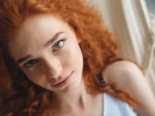 Primer plano de una joven con cabello castaño pelirrojo natural y ojos azules, recostada en una hamaca.