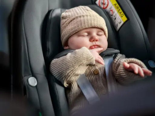 Śpiące dziecko w foteliku, bezpieczne dzięki 3 punktowym pasom bezpieczeństwa.