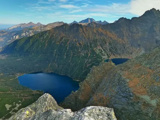 Widok na Tatry z góry. Na pierwszym planie skały, w dole las i jezioro Morskie Oko.