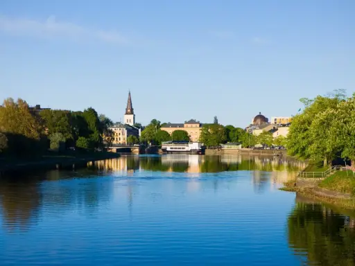Vacker vy över Klarälven i Karlstad med stadens silhuett och grönska. Perfekt för promenader och andra aktiviteter Karlstad erbjuder.