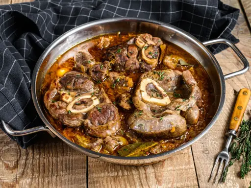Ossobuco que es: jugosas rodajas de ternera cocinadas a fuego lento en una rica salsa con hierbas y especias, servidas en una sartén metálica.
