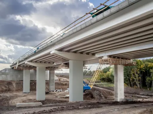 Construcción de un puente de viga con pilares de hormigón y grúa amarilla en el sitio.