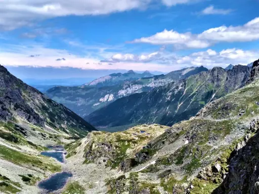 Majestatyczne Tatry Wysokie z doliną, dwoma stawami i skalistymi szczytami pod błękitnym niebem.