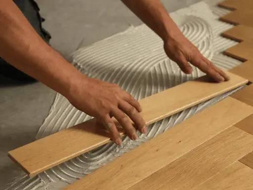 Man's hands carefully placing a wooden plank during the installation of floating flooring.