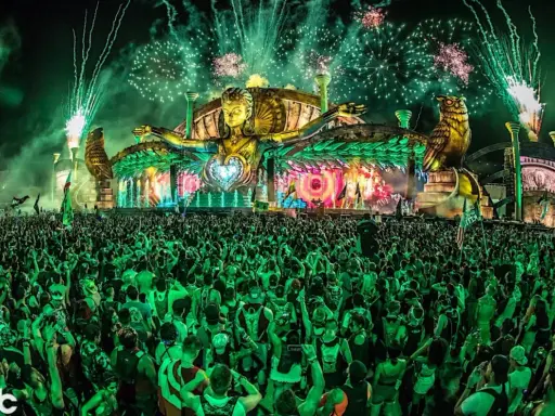 Folla immensa sotto un palco spettacolare con fuochi d'artificio verdi, uno dei rave party più famosi al mondo.