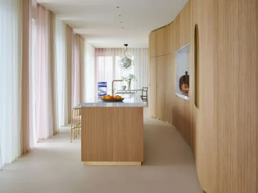 Interno moderno con isola cucina in legno e boiserie curvilinea. Tende leggere color pastello creano un'atmosfera soffusa.